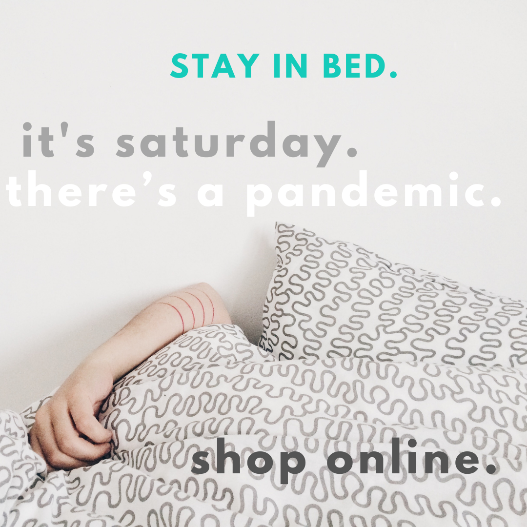 This is a picture of a person's in bed. You only see a hand peeking out from behind the comforter. The Words o top say "Stay In Bed. It's Saturday. There's a Pandemic." On the bottom, it reads "Shop Online." 